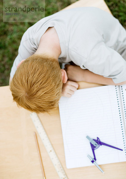 Junge mit Kopf auf Tisch neben geöffnetem Notizbuch