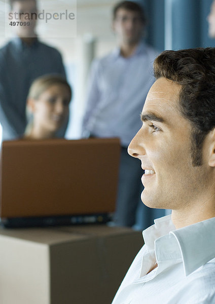 Junger Mann lächelnd  Profil  Kollegen mit Laptop im Hintergrund