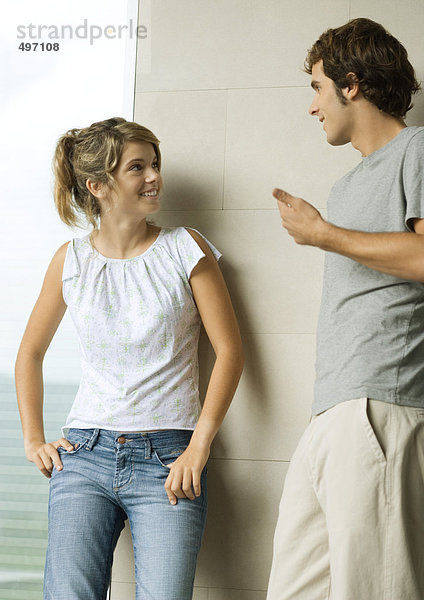 Junger Mann und Frau lehnen sich an die Wand  reden und lächeln