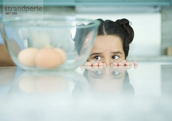 Mädchen schaut über den Rand der Theke auf Eier in der Rührschüssel