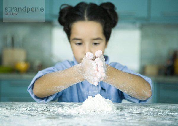 Mädchen steht an der Küchentheke und hält die Hände über dem Mehlhaufen.