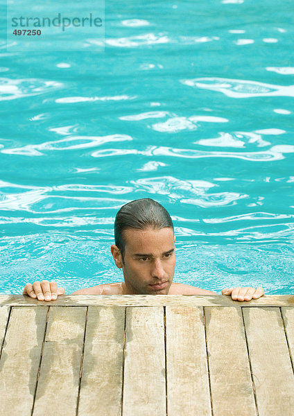 Mann im Pool stehend mit Händen an der Kante