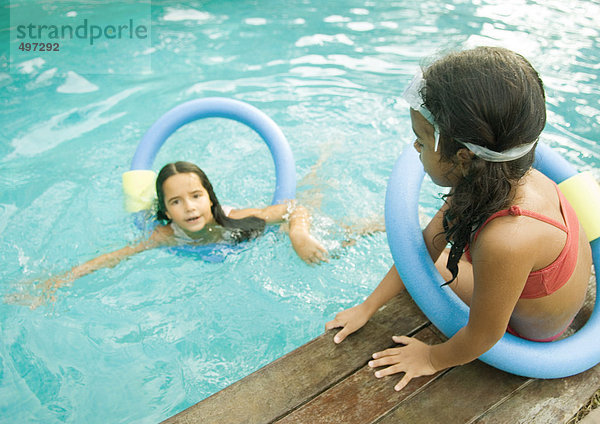 Zwei Mädchen mit schwimmenden Ringen  eines im Pool  eines am Beckenrand sitzend