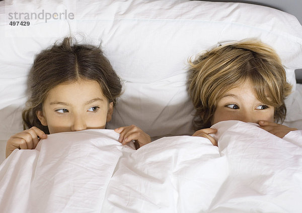 Zwei Kinder im Bett liegend mit bis zur Nase hochgezogener Decke