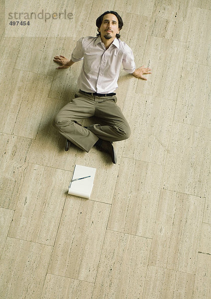 Mann auf dem Boden sitzend mit Papierblock vor sich  zurücklehnend  hohe Blickwinkel