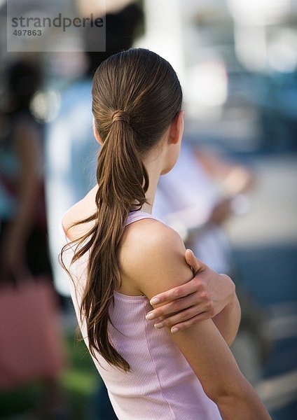 Junge Frau stehend mit Hand am Arm  Rückansicht