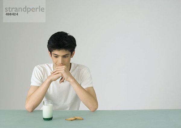 Junger Mann schaut auf ein Glas Milch und Kekse.