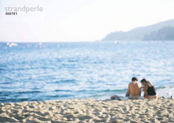 Zwei Menschen sitzen zusammen am Strand