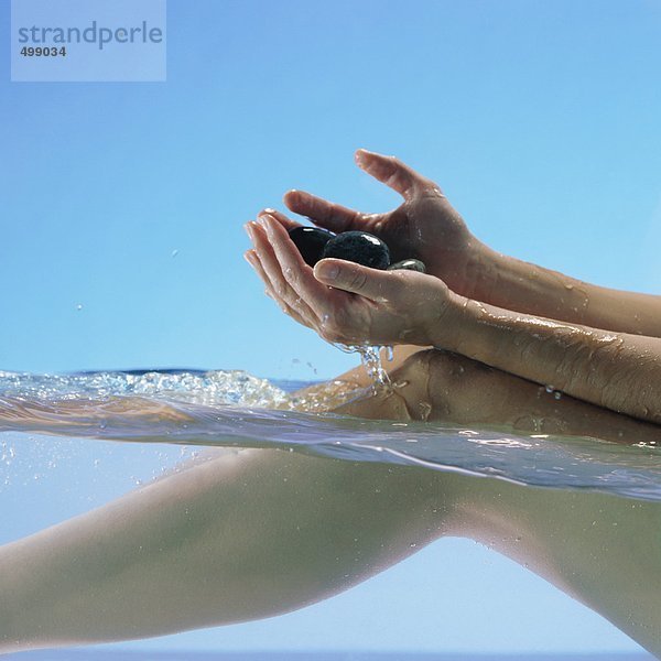 Frau im Wasser sitzend  Steine haltend  Beine und Hände zumachend