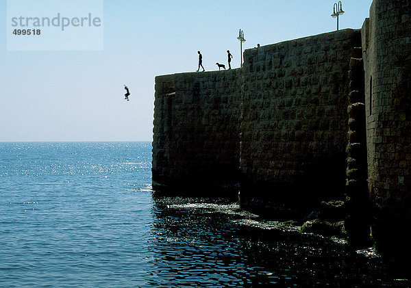 Menschen  die von der Steinmauer ins Meer springen.