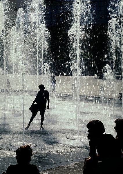 Person silhouettiert  unter Springbrunnen stehend
