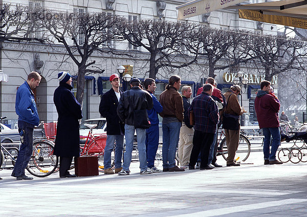 Gruppe von Leuten  die für kaltes Wetter gekleidet sind und auf dem Bürgersteig Schlange stehen.