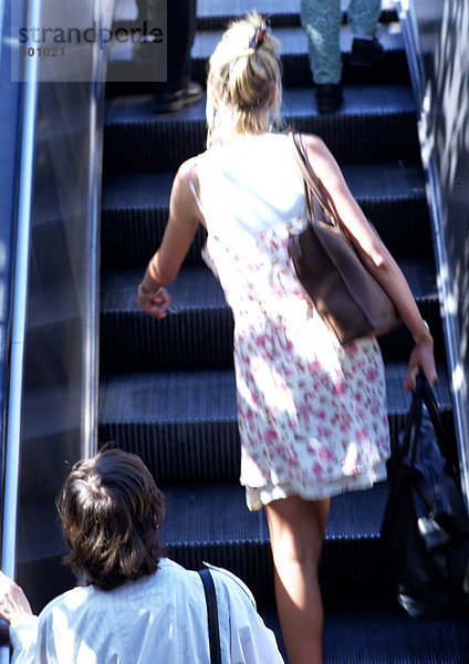 Frau geht die Rolltreppe hoch  Rückansicht.