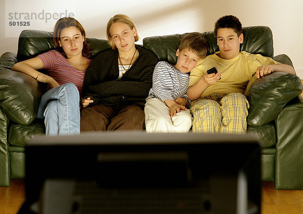 Fokus auf junge Erwachsene und Kinder  die im Hintergrund auf der Couch sitzen  Rückansicht des Fernsehers im Vordergrund  verschwommen.