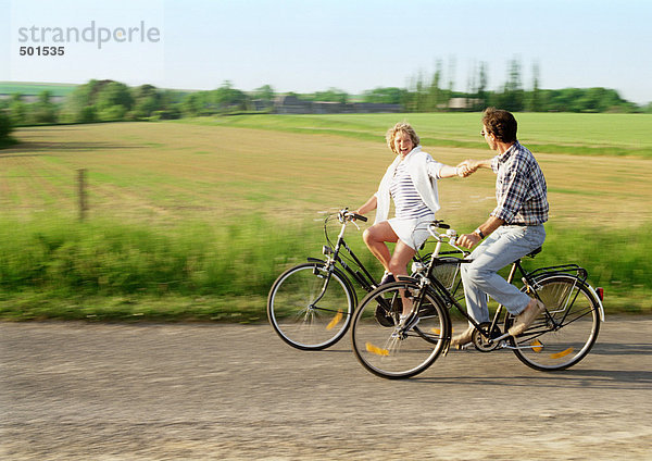 Mann und Frau beim Radfahren  Händchenhalten  Landschaft im Hintergrund