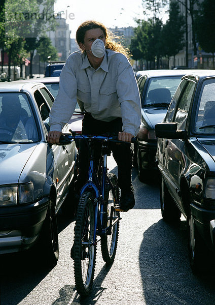 Person  die zwischen den Autos Fahrrad fährt  mit aufgesetzter Verschmutzungsmaske.