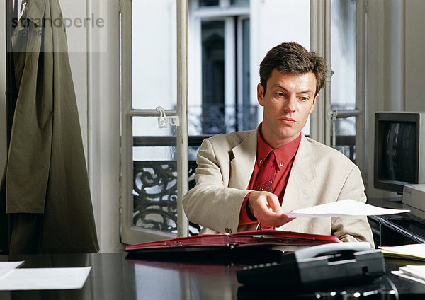 Mann am Schreibtisch sitzend  Papier haltend