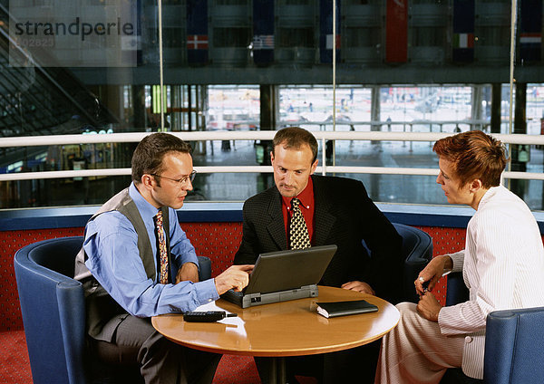 Zwei Männer und eine Frau sitzen am Tisch und schauen auf den Laptop.