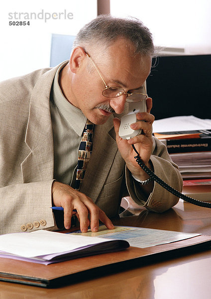Mann sieht sich Dokumente an  während er das Telefon benutzt.