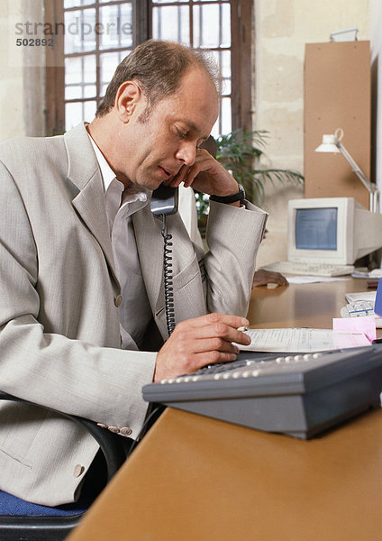 Mann am Schreibtisch sitzend  telefonierend  Seitenansicht