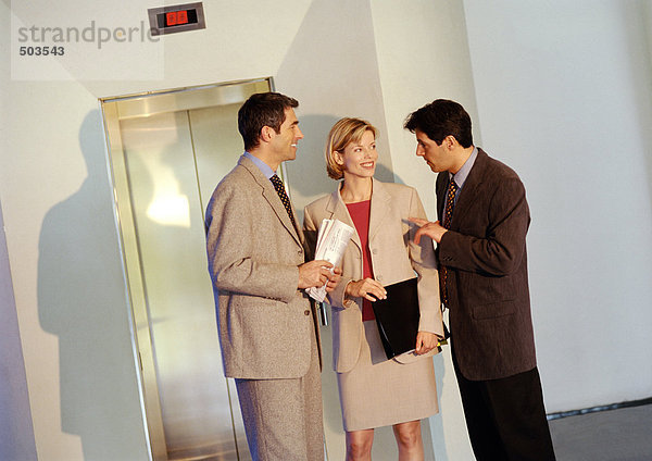 Zwei Geschäftsmänner und eine Geschäftsfrau stehen vor dem Aufzug