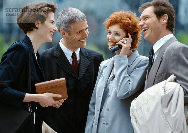 Vier Geschäftsleute stehen draußen lächelnd  Geschäftsfrau am Handy