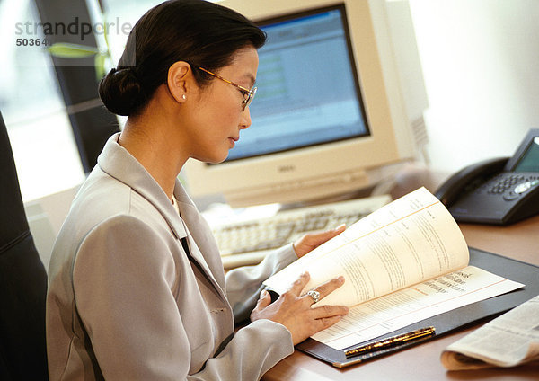 Geschäftsfrau am Schreibtisch sitzend  Dokument lesen  Seitenansicht