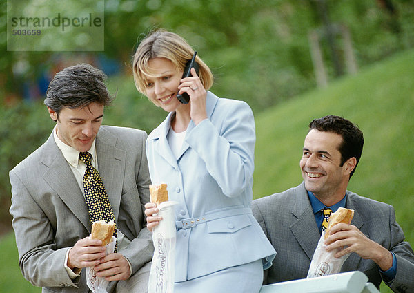 Drei Geschäftsleute mit Sandwiches im Freien  einer mit Handy