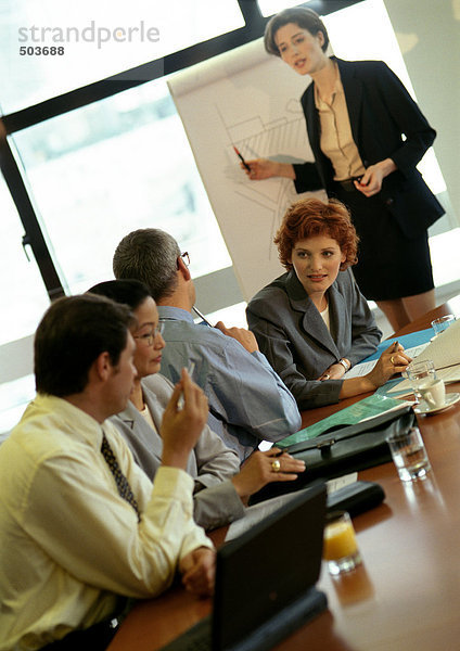 Vier Geschäftsleute sitzen  Geschäftsfrau zeigt auf das Brett im Hintergrund