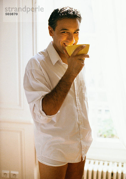 Mann in Buttondown-Shirt und Unterwäsche  Schale an Mund haltend  lächelnd