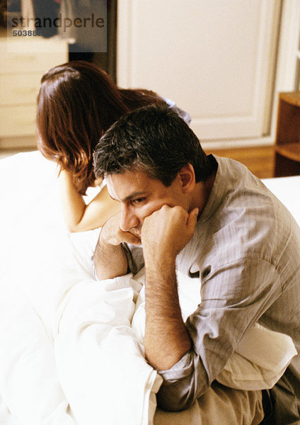 Mann und Frau im Bett sitzend  Köpfe an den Händen lehnend  Taille hoch  Seitenansicht