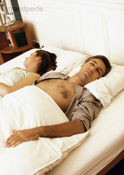 Im Bett liegendes Paar mit gegenläufig gedrehten Köpfen
