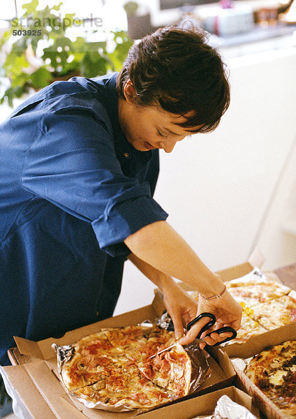 Frau schneidet Pizzascheiben mit Schere  Taille hoch