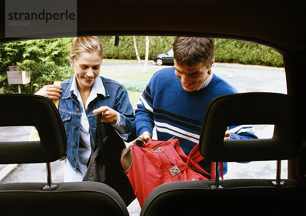 Mann und Frau legen Taschen in den Kofferraum  Kopfstützen im Vordergrund
