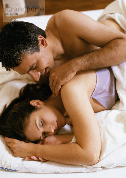 Paar im Bett liegend  Mann berührt die Schulter der Frau