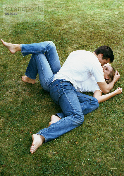 Paar auf Gras liegend  Mann lehnt sich über Frau