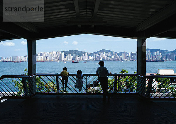 Hongkong  Silhouetten eines Erwachsenen mit zwei Kindern auf der Schiene  Rückansicht  Stadt in der Ferne