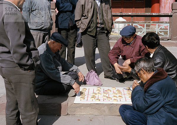 China  Provinz Xinjiang  Urumqi  Gruppe von Männern  die auf dem Bürgersteig sitzen und Xiangi auf dem Bürgersteig spielen.