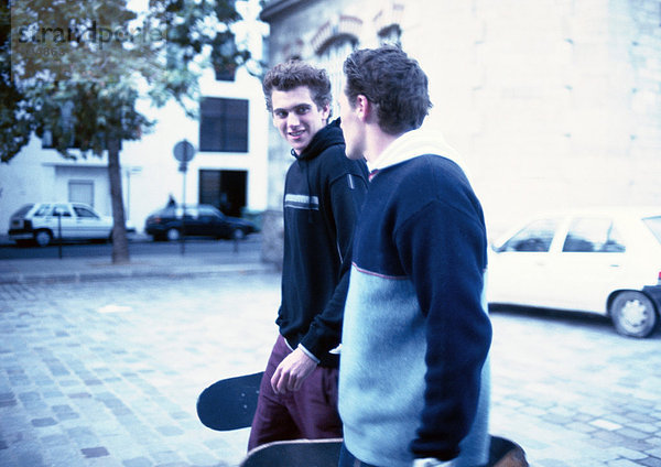 Zwei junge Männer  die auf der Straße laufen und Skateboards halten.