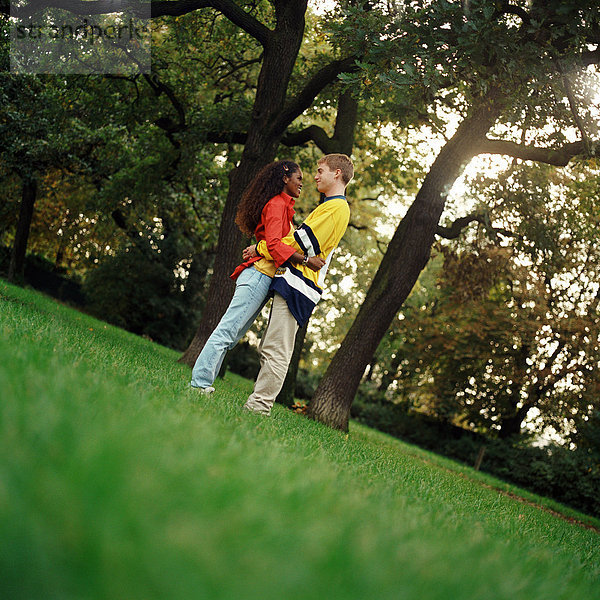 Junger Mann und Frau auf Gras stehend  umarmend  Seitenansicht  volle Länge