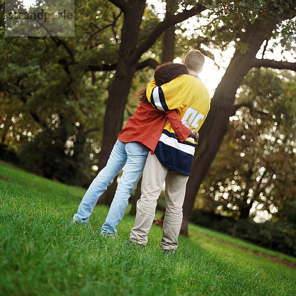 Junger Mann und Frau auf Gras stehend  umarmend  Rückansicht  volle Länge