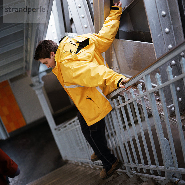 Teenager-Junge im Regenmantel  der im Treppenhaus nach unten rutscht.