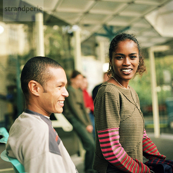 Junge Frau und junger Mann sitzen zusammen am Busbahnhof