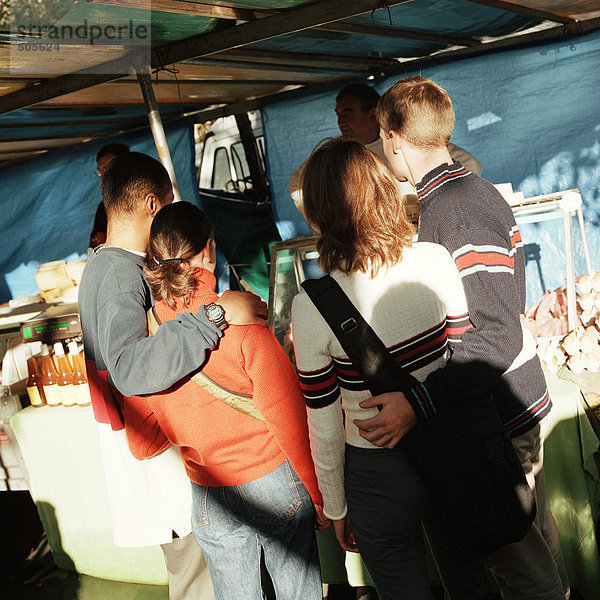 Junge Paare mit Armen umeinander  auf dem Straßenmarkt stehend  Rückansicht