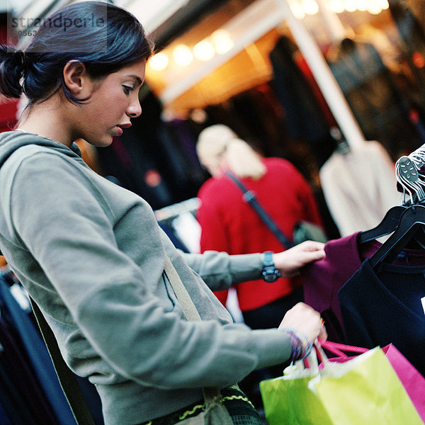 Teenagermädchen schaut auf Kleiderständer  hält Einkaufstaschen  draußen