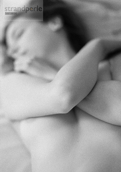 Nackte Frau auf dem Bett liegend  Arme über der Brust verschränkt  Nahaufnahme  schwarz-weiß.