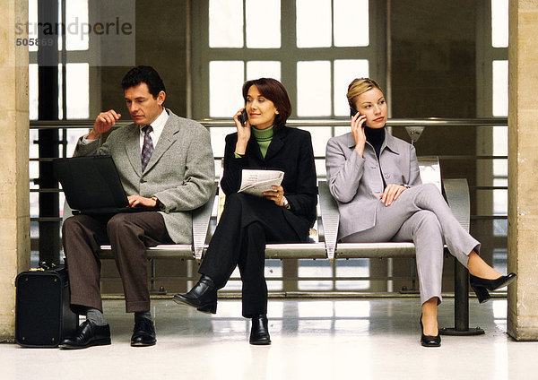 Geschäftsfrauen  die Handys benutzen  sitzen neben einem Geschäftsmann mit Laptop.