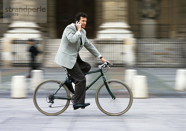 Mann im Anzug  hält Handy an Ohr und Fahrrad  verschwommen.