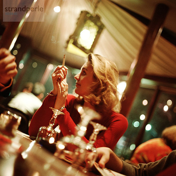 Junge Frau mit Zigarette und Blick über die Schulter auf den Tisch im Restaurant