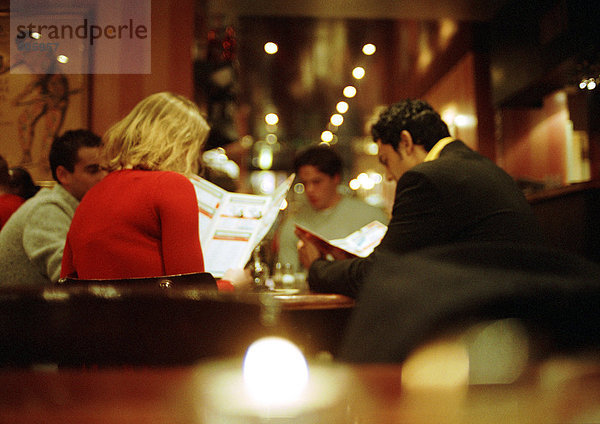 Gruppe junger Leute  die im Restaurant sitzen und sich die Menüs anschauen